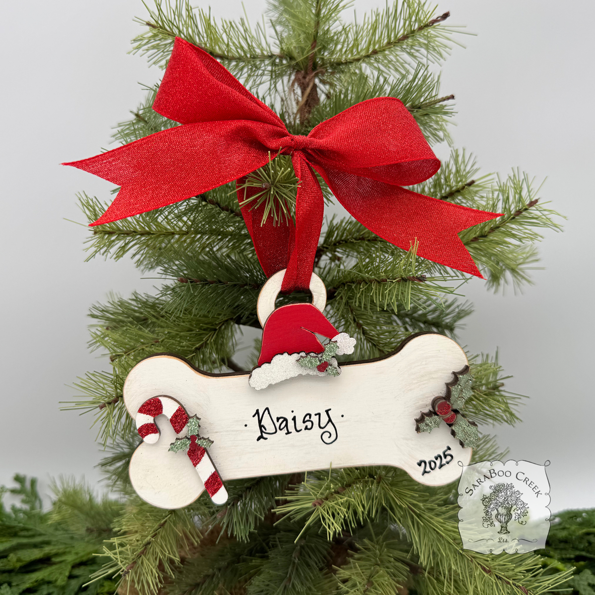 Decorative Christmas ornament with a red bow, bone-shaped tag, and 'Daisy 2025' text on a tree.