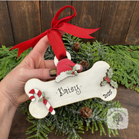 Hand holding a personalized dog bone ornament with a red ribbon against a wooden background.