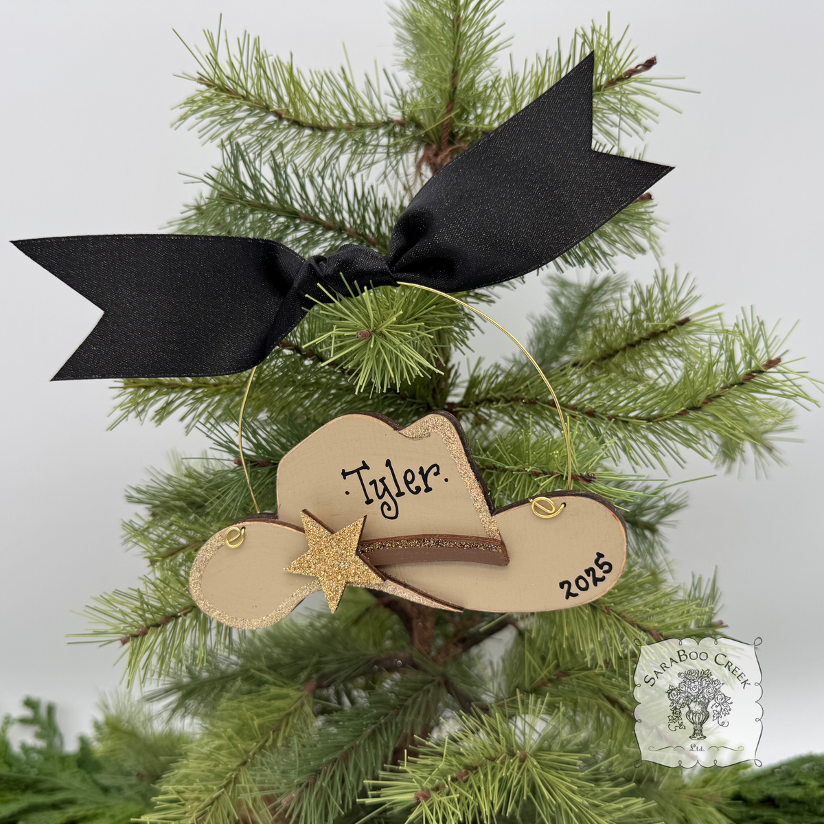 Decorative wood ornament shaped like a cowboy hat with a black bow on a Christmas tree.